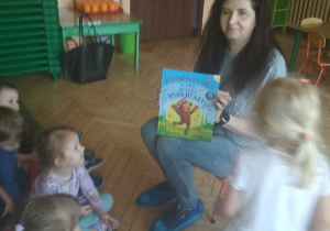 Zdjęcie przedstawia panią bibliotekarkę, która pokazuje dzieciom książeczkę, którą przyniosła ze sobą.