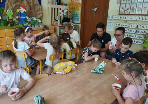 Zdjęcie przedstawia dzieci wraz z rodzicami podczas spożywania galaretki z truskawakmi.