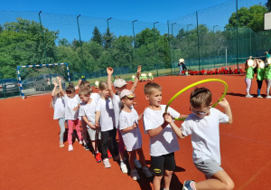 Zdjęcie przedstawia dzieci w konkurencji - przekładanie hula hop do tyłu nad głową na czas.