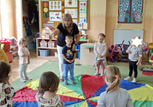 Zdjęcie przedstawia dzieci biorące udział w zabawie z wykorzystaniem chusty animacyjnej "Kolory".
