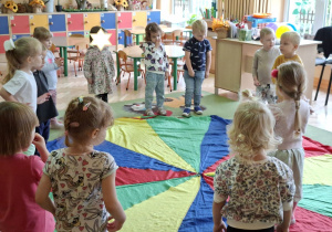 Zdjęcie przedstawia dzieci biorące udział w zabawie z wykorzystaniem chusty animacyjnej "Kolory".