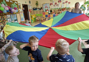 Zdjęcie przedstawia dzieci biorące udział w zabawie z wykorzystaniem chusty animacyjnej "Imiona".