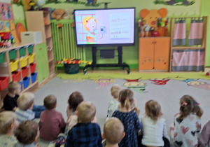 Zdjęcie przedstawia dzieci z grupy I i II oglądające na monitorze interaktywnym film edukacyjny 'Pierwsza pomoc".