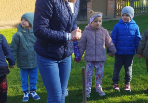 Zdjęcie przedstawia dzieci oraz prowadzącą, która opowiada, w jaki sposób dawniej wyrabiano masło i jakich narzędzi do tego używano.