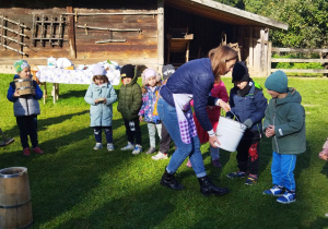 Na tym zdjęciu widać prowadzącą, która pokazuje dzieciom mleko, z którego będą wyrabiały masło.