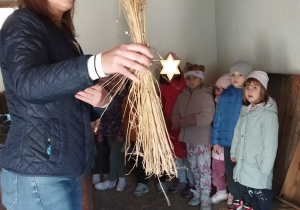 Zdjęcie przedstawia dzieci oraz prowadzącą opowiadającą o różnych rodzajach zbóż.