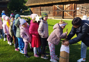 Zdjęcie przedstawia dzieci, które próbują swoich sił w ubijaniu masła w maselnicy.