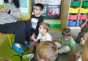 Zdjęcie przedstawia panią bibliotekarkę czytającą dzieciom książeczkę oraz słuchające dzieci.