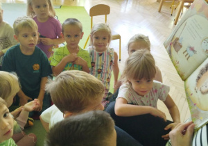 Zdjęcie przedstawia dzieci słuchające książeczki czytanej przez panią bibliotekarkę.