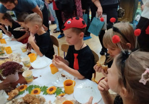 Zdjęcie przedstawia kilkoro dzieci siedzących przy stole podczas poczęstunku.