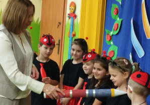 Zdjecie przedstawia kilkoro dzieci oraz panią dyrektor, która pasuje je na przedszkolaka w grupie "Biedronek".