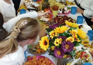 Zdjęcie przedstawia dzieci siedzące przy stole z różnymi przekąskami.