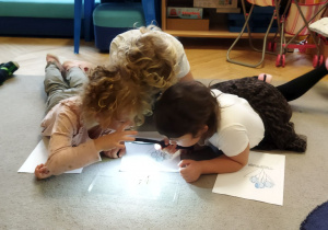 Na tym zdjęciu widać troje dzieci obserwujących nasiona przez lupę.