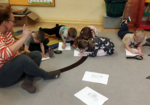 Zdjęcie przedstawia mamę prowadzącą zajęcia oraz dzieci kolorujące malowanki z roślinami.