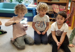 Zdjęcie przedstawia Oliwię oglądającą przez podświetlaną lupę nasiona oraz inne dzieci.