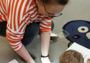 Na tym zdjęciu widać mamę prowadzącą warsztaty oraz jednego z chłopców obserwującego przez lupę nasionka.