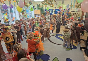 Na tym zdjęciu widać przedszkolaki poruszające się korowodem przy dźwiękach jesiennej piosenki.