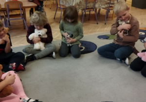 Zdjęcie przedstawia kilkoro dzieci siedzące na dywanie z misiami podczas zajęcia.