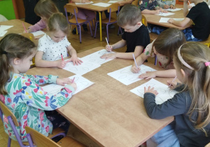 Zdjęcie przedstawia kolejną grupkę dzieci tworzących szkice, przekształcając podane wzory.