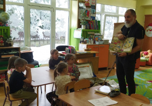 Zdjęcie przedstawia kilkoro dzieci i ilustratora opowiadającego o swojej pracy.