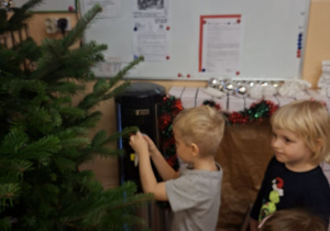 Zdjęcie przedstawia Asię, Anielkę i Mikołaja L., który wiesza ozdobę na choinkę.