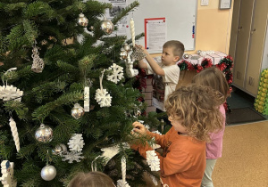 Zdjęcie przedstawia dzieci z grupy III ubierające choinkę.