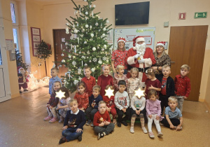 Zdjęcie przedstawia dzieci z grupy I wraz z paniami i MIkołajem przy choince.
