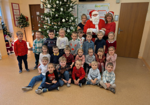 Zdjęcie przedstawia dzieci z grupy II wraz z paniami i MIkołajem przy choince.