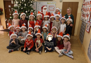 Zdjęcie przedstawia dzieci z grupy IV wraz z paniami i MIkołajem przy choince.