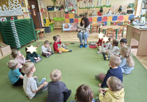 Zdjęcie przedstawia wszystkie dzieci słuchające bajki czytanej przez panią bibliotekarkę.