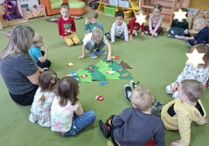 Na tym zdjęciu widać Damiana, który umieszcza ozdobę według polecenia nauczycielki - na dole choinki oraz pozostałe dzieci.