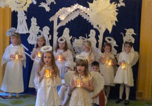 Na tym zdjęciu widać dziewczynki w roli aniołków śpiewające piosenkę z wykorzystaniem latarenek.