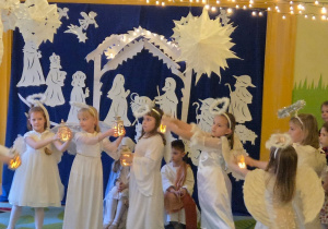 Zdjęcie przedstawia dziewczynki w roli aniołków wykonujące taniec z latarenkami.
