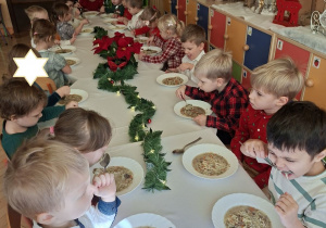 Na tym zdjęciu widać dzieci spożywające wigilijną zupę przy wspólnym stole.
