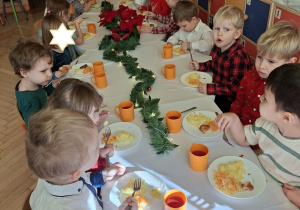 Na tym zdjęciu widać dzieci spożywające drugie danie z rybą przy wspólnym stole.
