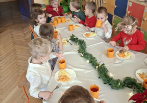 Na tym zdjęciu widać dzieci spożywające drugie danie z rybą przy wspólnym stole.