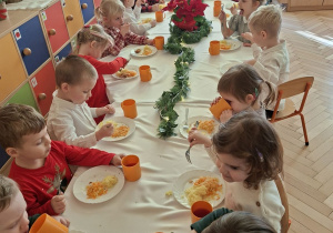 Zdjęcie przedstawia dzieci podczas posiłku przy wspólnym, świątecznie udekorowanym stole.