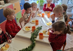 Zdjęcie przedstawia dzieci podczas posiłku przy wspólnym, świątecznie udekorowanym stole.