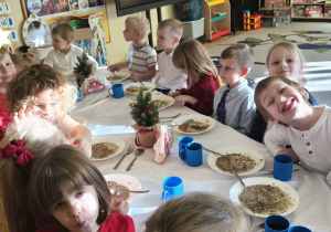 Zdjęcie przedstawia dzieci spożywające wigilijną zupę przy wspólnym, świątecznym stole.