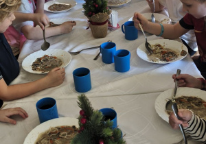 Zdjęcie przedstawia dzieci spożywające wigilijną zupę przy wspólnym, świątecznym stole.