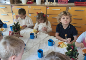 Na tym zdjęciu widać dzieci spożywające drugie danie z rybą przy wspólnym stole.