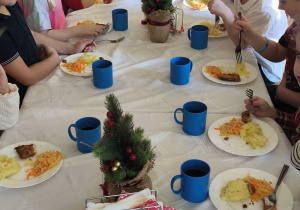 Na tym zdjęciu widać dzieci spożywające drugie danie z rybą przy wspólnym stole.