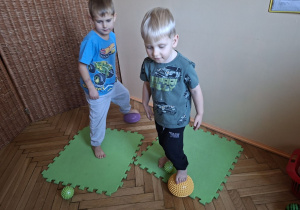 Na tym zdjęciu widać Tymona z grupy III oraz Henia D. z grupy I wykonujących ćwiczenia stóp z wykorzystaniem jeżyków.