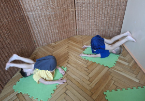 Na tym zdjeciu widać dwoje dzieci z grupy III podczas przenoszenia nóg za głowę w pozycji leżenie tyłem.