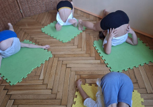 Na tym zdjeciu widać czworo dzieci z grupy IV podczas przenoszenia nóg za głowę w pozycji leżenie tyłem.