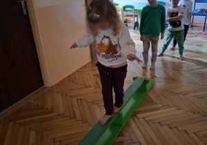Na tym zdjęciu wdać dzieci z grupy II wykonujące ćwiczenia rónoważne z wykorzystaniem ławeczki gimnastycznej.