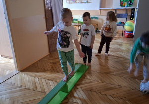 Na tym zdjęciu wdać dzieci z grupy II wykonujące ćwiczenia rónoważne z wykorzystaniem ławeczki gimnastycznej.
