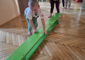 Na tym zdjęciu wdać dzieci z grupy II wykonujące ćwiczenia zwinnościowe z wykorzystaniem ławeczki gimnastycznej.