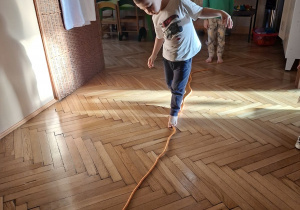 Zdjęcie przedstawia dzieci z grupy II wykonujące ćwiczenia stóp połączone z ćwiczeniami równoważnymi z wykorzystaniem liny.