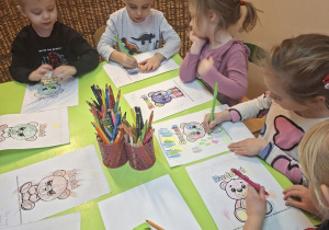 Zdjęcie przedstawia Mikołaja L. z grupy I oraz czworo dzieci z grupy II, które kolorują misie wyrażające minką różne stany emocjonalne.